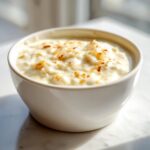 Close-up of a creamy white pizza sauce, flecked with browned spices, served in a small white bowl.