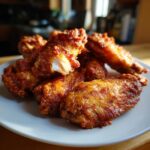 A close-up of several golden-brown, crispy baked chicken wings piled on a white plate, showing the texture.