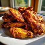 A close-up of a pile of golden brown, crispy chicken wing pieces served on a white plate.