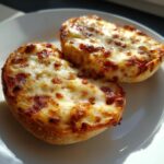 Close-up of two halves of golden brown English muffin pizza topped with bubbly, melted cheese.