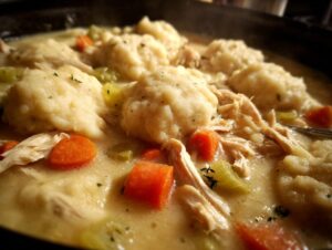 Close-up shot of steaming, creamy chicken and dumplings, featuring shredded chicken, carrots, and celery.