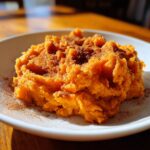 A close-up of creamy, bright orange mashed sweet potatoes topped generously with ground cinnamon.