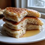 Close-up of a stack of fluffy sourdough pancakes, cut open to show the airy interior, drizzled with syrup.