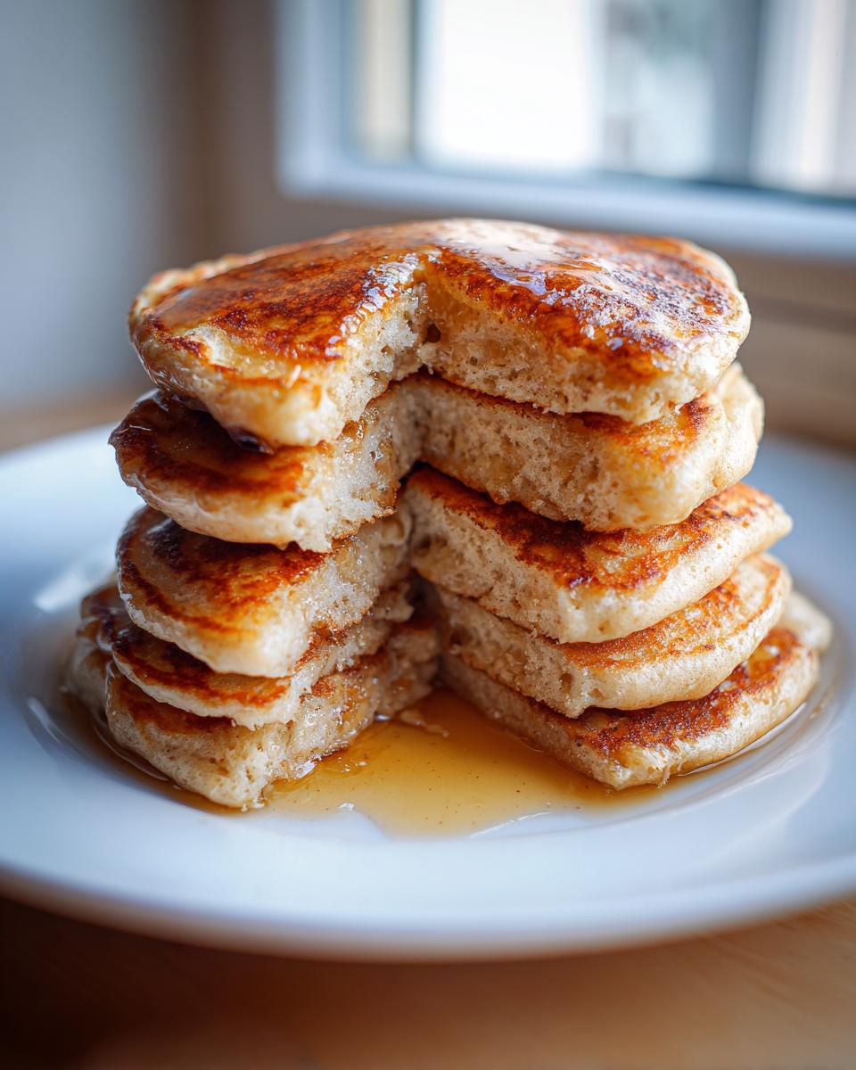 A tall stack of fluffy sourdough pancakes, cut open to show the interior texture, drizzled with syrup.