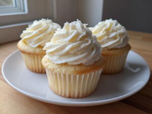 Three moist vanilla cupcakes topped with swirls of rich white vanilla buttercream frosting on a white plate.