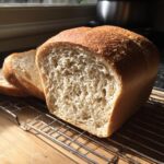 Close-up of a freshly baked loaf of fluffy whole wheat bread, sliced and resting on a wire cooling rack.
