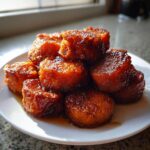 A stack of glistening, brown candied sweet potatoes covered in thick syrup on a white plate.