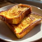 Two golden brown slices of crispy, custardy french toast stacked on a white plate.