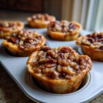 Close-up of several gooey mini pecan pies cooling in a metal muffin tin.
