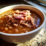 Close-up of a white bowl filled with rich Ham and bean soup, topped generously with shredded ham.