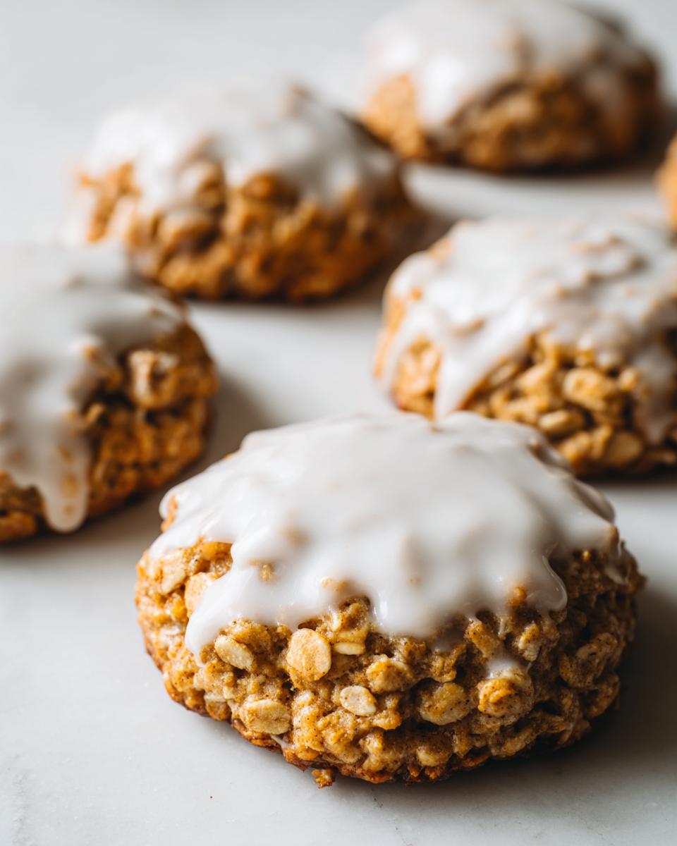 A close-up of a soft, chewy iced oatmeal cookies topped with a thick layer of white vanilla glaze.