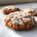 Close-up of a soft, textured iced oatmeal cookie topped with a thick white glaze.