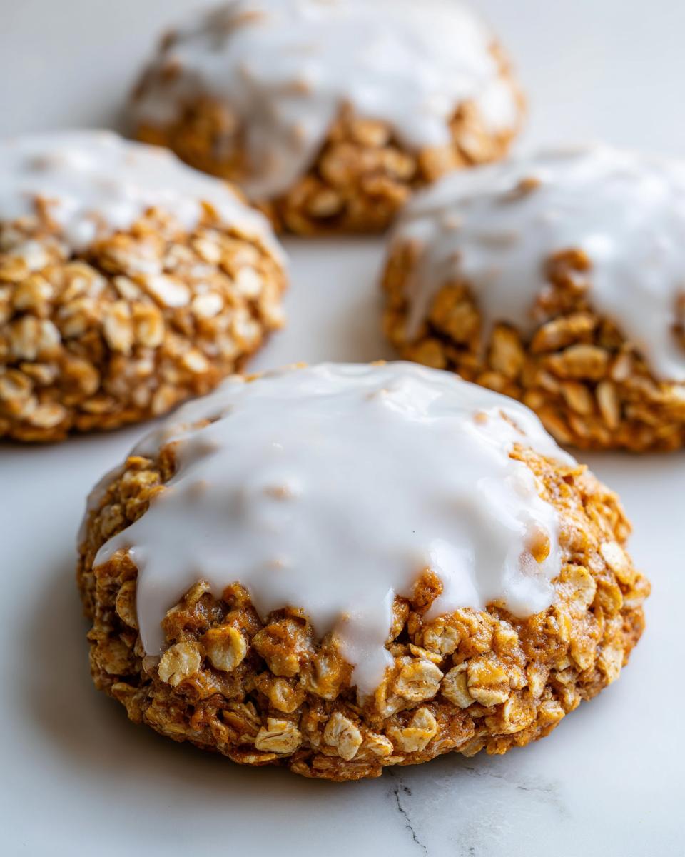 A close-up of a soft, chewy iced oatmeal cookies topped with thick white vanilla glaze.