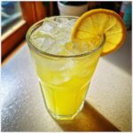 A tall glass filled with bright yellow, icy homemade lemonade garnished with a fresh lemon slice.