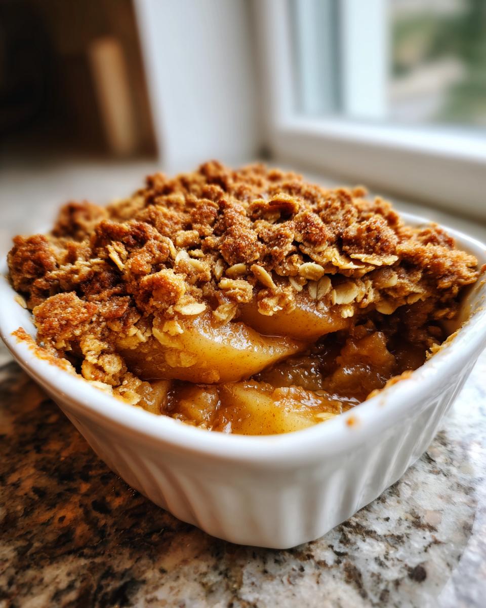 A close-up of a warm, individual serving of pear crisp with a thick, golden-brown oat topping and soft, spiced pears underneath.