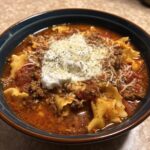 A close-up of a bowl of rich instant pot lasagna soup topped with a dollop of ricotta cheese and shredded parmesan.