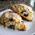 Close-up of two delicious lemon blueberry scones topped with a thick, dripping lemon glaze.
