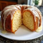A sliced lemon pound cake with a thick, white glaze dripping down the sides onto a white plate.