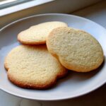 Three golden brown sugar cookie rounds sprinkled with coarse sugar, resting on a light gray plate.