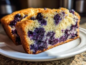 Close-up of two thick slices of moist blueberry bread showing a tender crumb packed with deep purple blueberries.