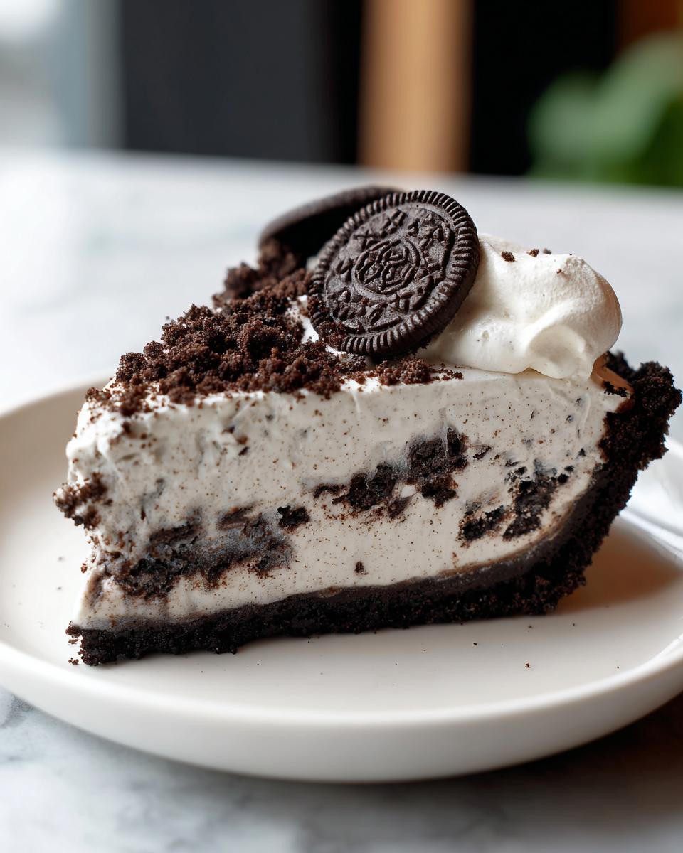 A close-up of a decadent slice of no bake oreo pie showing the creamy filling, dark crust, and cookie topping.