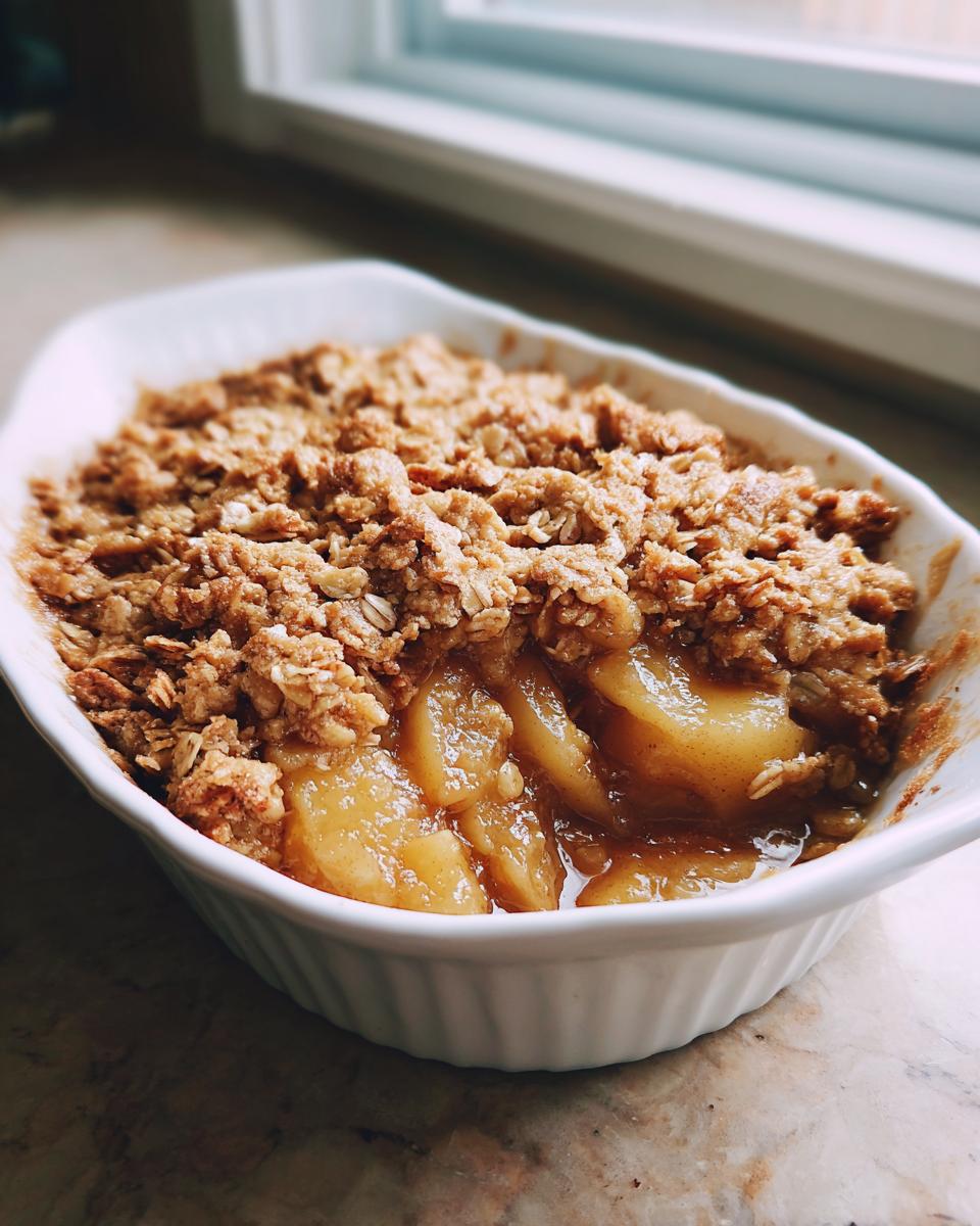 A close-up of a warm, bubbling pear crisp with a golden oat topping served in a white baking dish.
