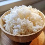 Close-up of perfectly cooked, glistening sushi rice piled high in a small wooden bowl.