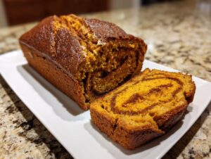 A loaf of pumpkin sourdough bread, partially sliced, revealing a rich orange interior and a dark cinnamon swirl pattern.