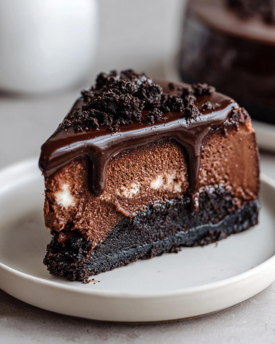 A decadent slice of chocolate cheesecake topped with shiny chocolate ganache and cookie crumbs.