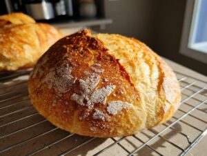 A golden-brown, round loaf of homemade french bread with a crackled, floured crust cooling on a wire rack.