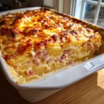 A close-up of a creamy, baked dish of scalloped potatoes and ham with a bubbly, golden-brown cheese crust.