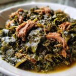 A close-up of tender, slow-cooked collard greens served in a white bowl topped with shredded smoked meat.