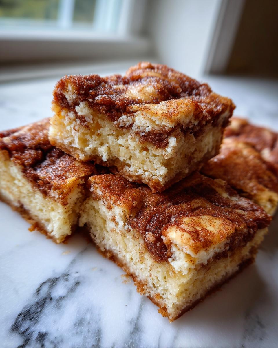 Close-up of stacked, soft snickerdoodle blondies squares with a rich cinnamon swirl topping on a marble surface.
