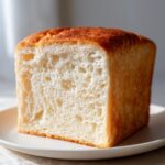 Close-up of a perfectly baked, square slice of incredibly soft milk bread showing its fluffy white interior and golden crust.