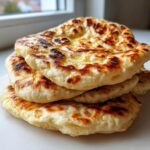 A stack of fluffy, freshly cooked naan bread recipe rounds with golden-brown, slightly charred spots and a buttery sheen.
