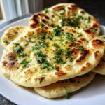 Close-up of soft skillet naan bread brushed with melted butter and topped with fresh chopped parsley.