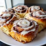 A close-up shot of several freshly baked sourdough discard cinnamon rolls topped with thick white icing.