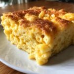 A close-up of a square slice of rich, creamy southern baked macaroni and cheese with a perfectly browned top.