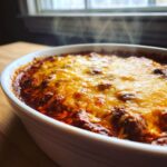 Close-up of steaming hot chili cheese dip with a thick layer of melted, bubbly orange cheese topping.