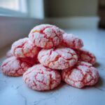 A stack of bright pink, crinkle-coated strawberry cake mix cookies resting on a white marble surface.