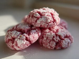 Close-up of three pink, crinkle-textured strawberry cake mix cookies dusted heavily with powdered sugar.