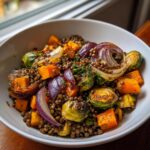 A bowl of warm veggie lentil salad featuring roasted butternut squash, Brussels sprouts, and red onion.