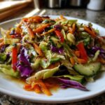 Close-up of a vibrant cabbage salad featuring shredded green and purple cabbage, carrots, cucumber, and red pepper tossed in a savory dressing.